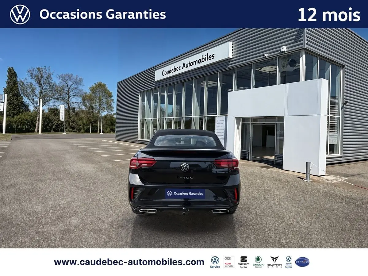 Vue arrière d'un Volkswagen T-Roc Cabriolet noir, avec attelage amovible et feux arrière LED, devant un showroom.