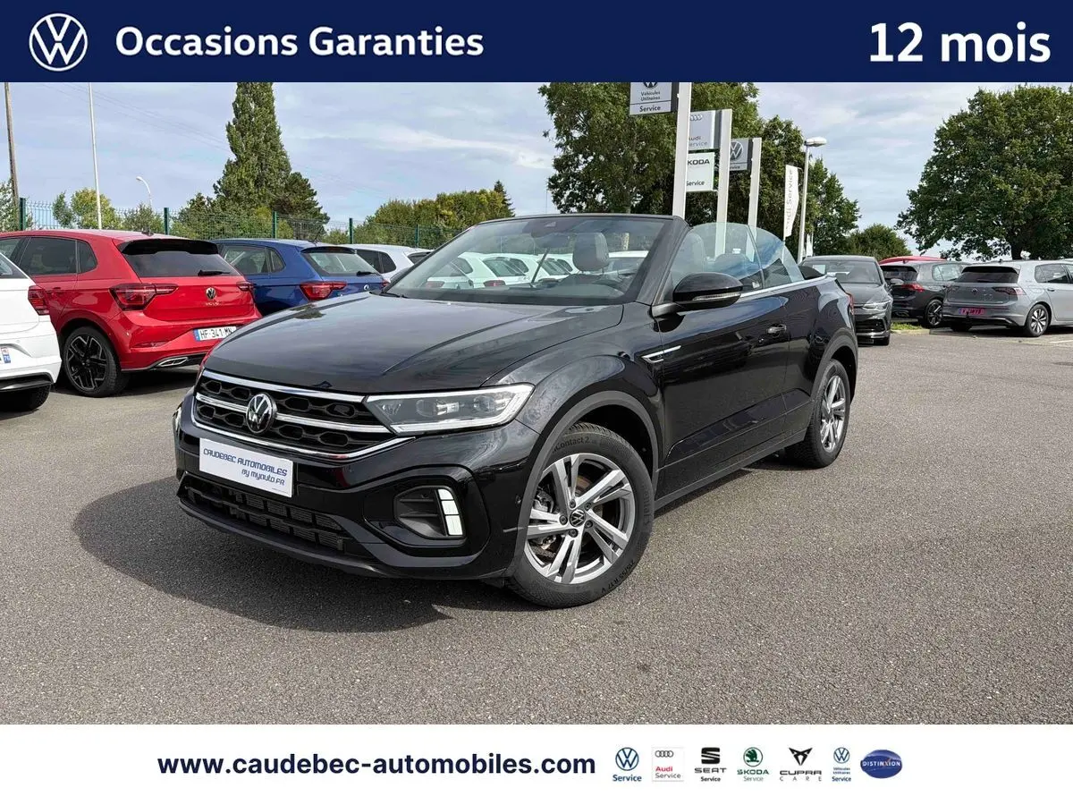 Volkswagen T-Roc Cabriolet noir en 3/4 avant droit sur parking, capote ouverte et jantes alliage visibles.