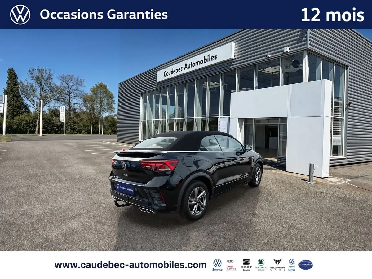 Volkswagen T-Roc Cabriolet noir vue 3/4 arrière droit, toit fermé, stationné devant un bâtiment moderne.