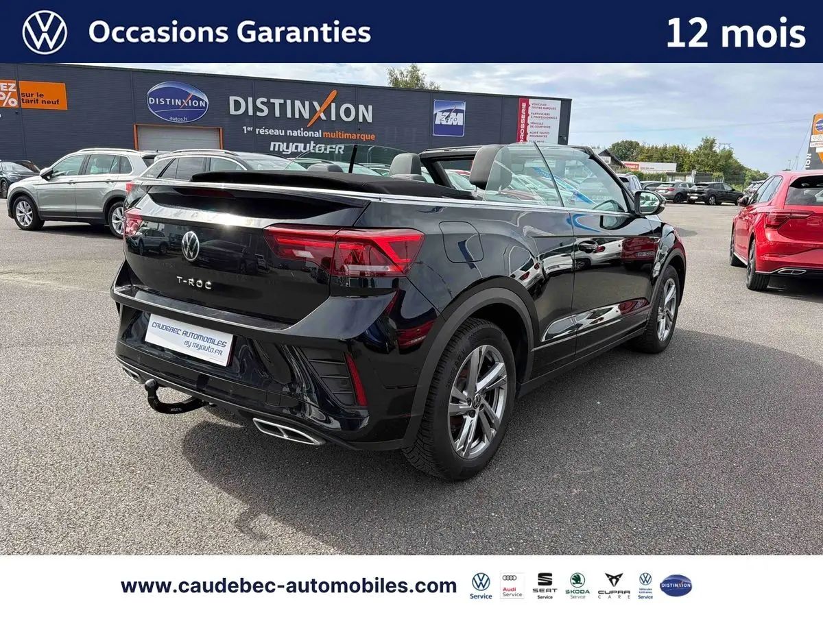 Volkswagen T-Roc Cabriolet noir vue 3/4 arrière droit avec attelage amovible sur parking extérieur.