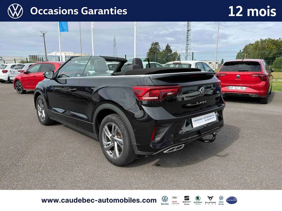 Volkswagen T-Roc Cabriolet noir vu en 3/4 arrière droit, toit ouvert, avec attelage amovible visible.