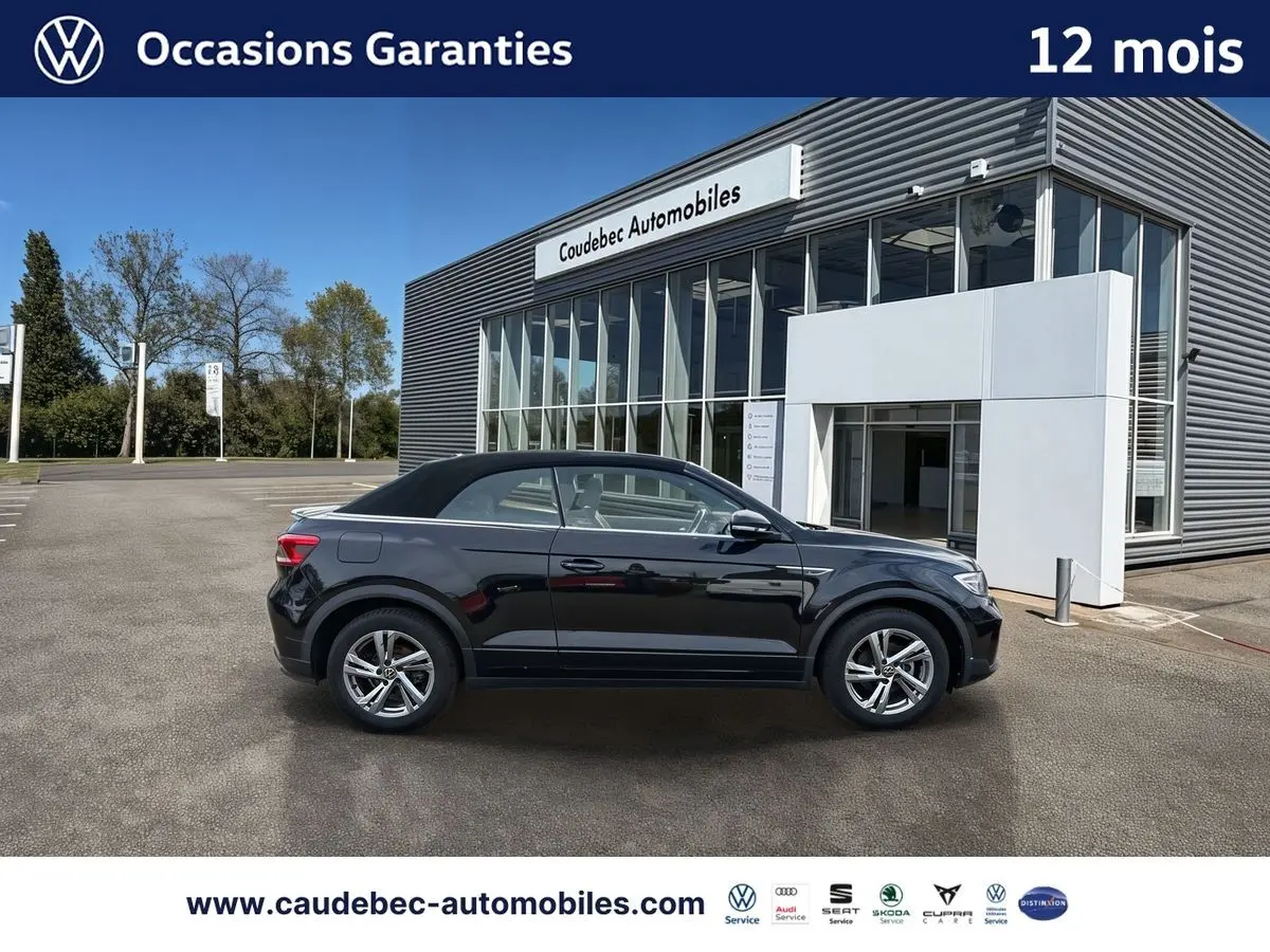 Profil droit du Volkswagen T-Roc Cabriolet noir avec toit fermé, garé devant un showroom moderne.