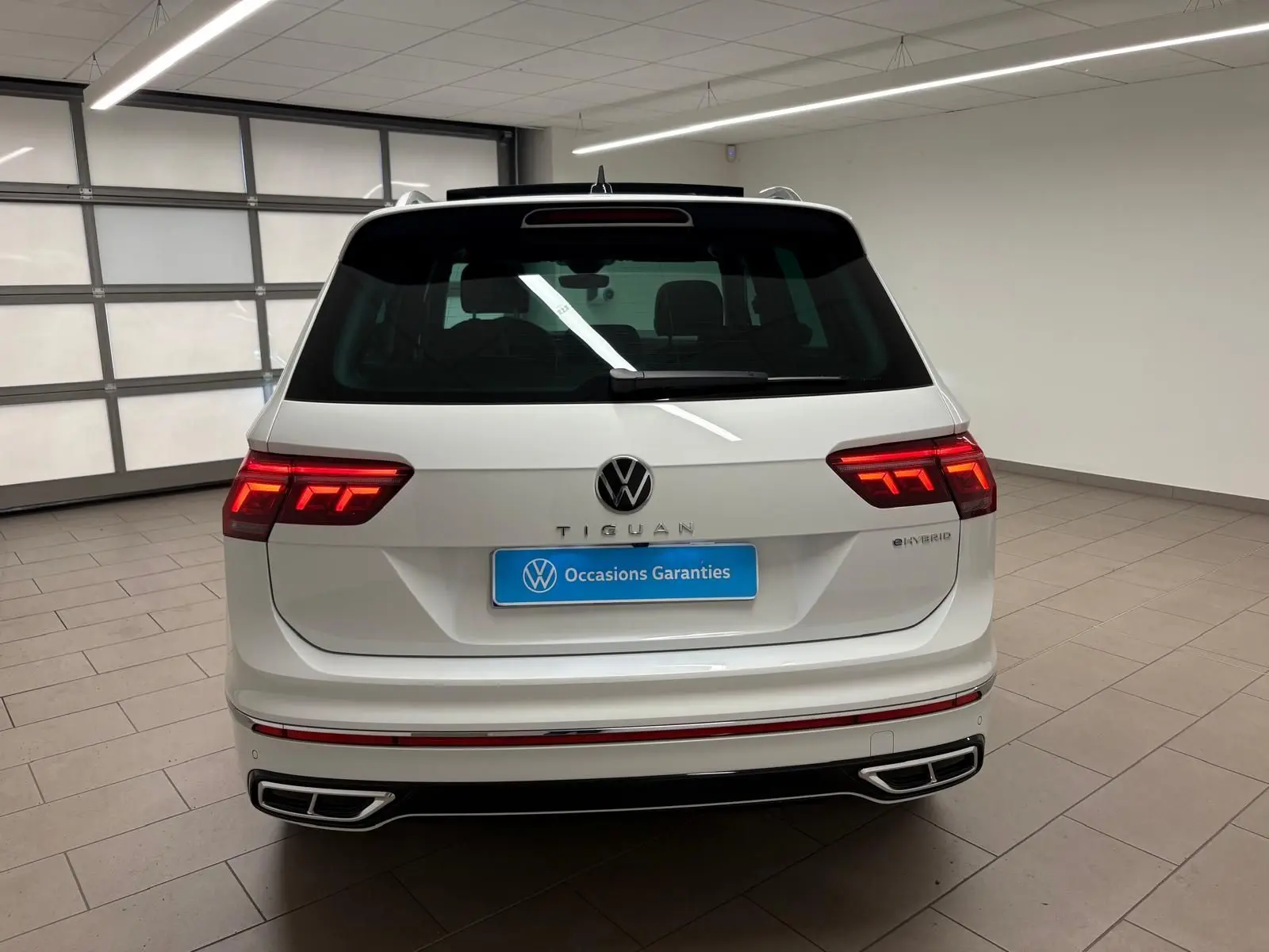 Vue arrière d'un Volkswagen Tiguan blanc pur 2023 hybride rechargeable avec feux LED et double sortie d'échappement intégrée.