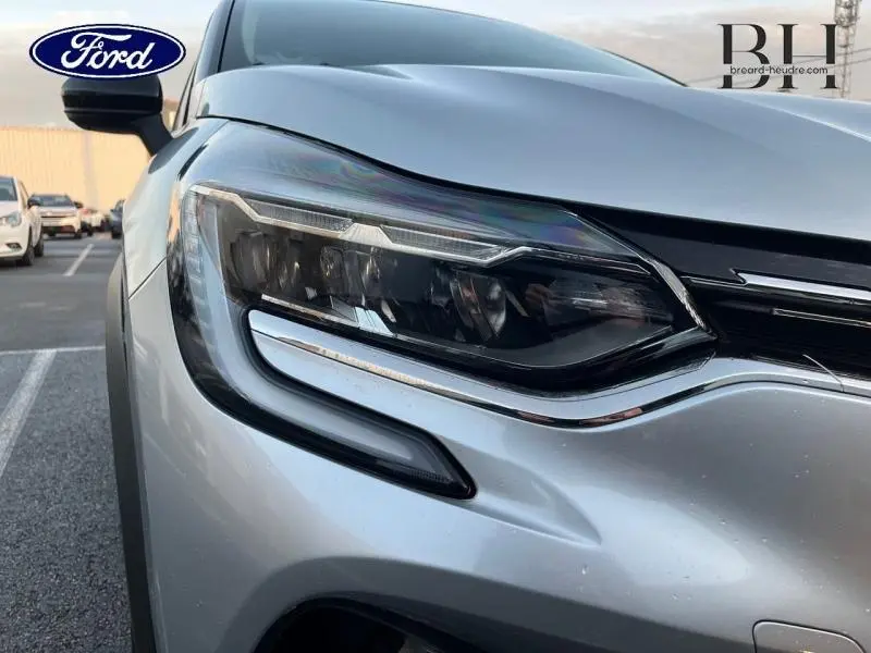 Gros plan sur le phare avant gauche du Renault Captur gris Highland avec détails chromés et contours noirs.