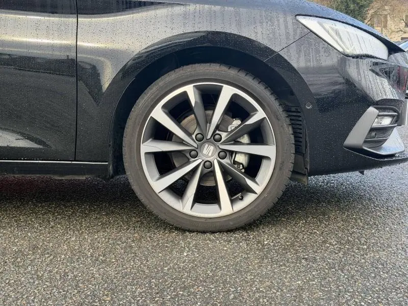 Gros plan sur la roue avant droite et la partie latérale noire métallisée du SEAT LEON ST 1.5 eTSI Hybrid 2025.