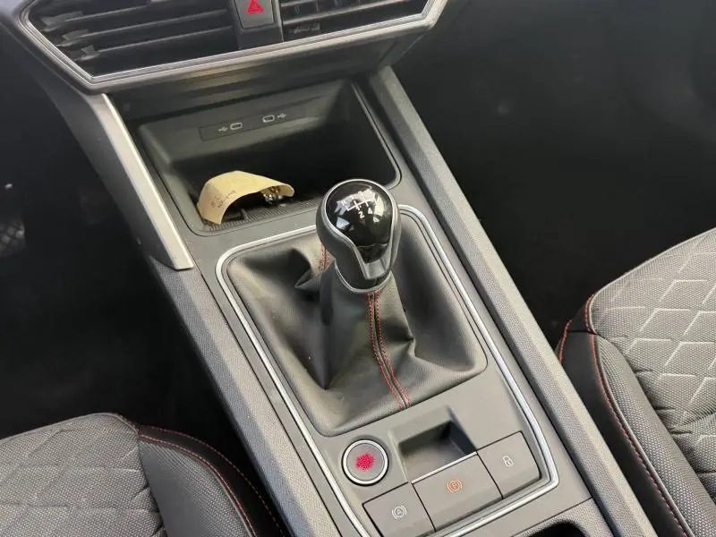 Gros plan sur la console centrale avec levier de vitesse manuel et surpiqûres rouges dans l’habitacle noir du SEAT LEON ST.