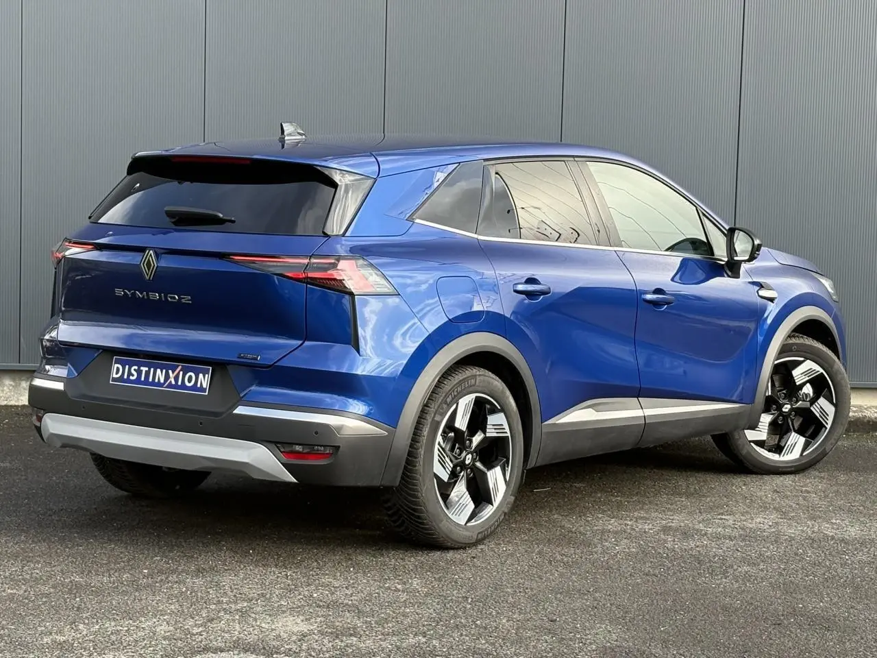 Renault Symbioz E-Tech hybride bleu Iron en 3/4 arrière droit, avec jantes 18 pouces et hayon mains libres.