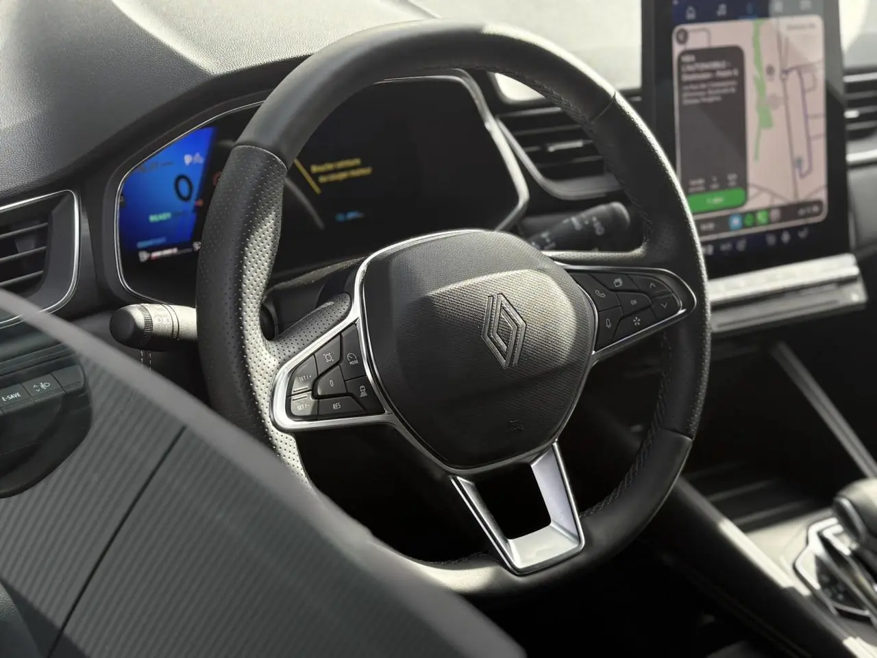 Vue rapprochée du volant noir perforé de la Renault SYMBIOZ avec écran numérique et console tactile visible en arrière-plan.
