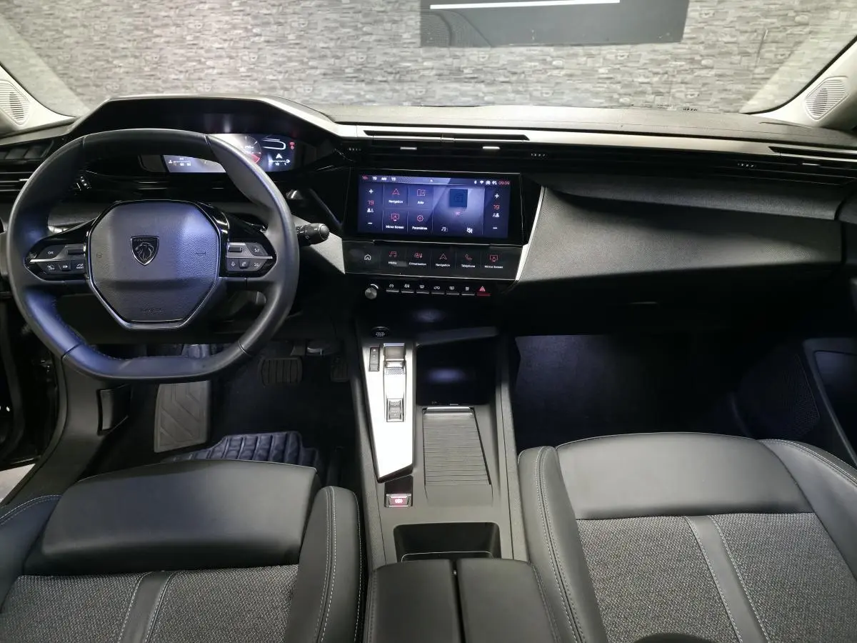 Vue intérieure avant de la Peugeot 308 SW 2024, tableau de bord noir avec écran tactile et volant cuir compact.