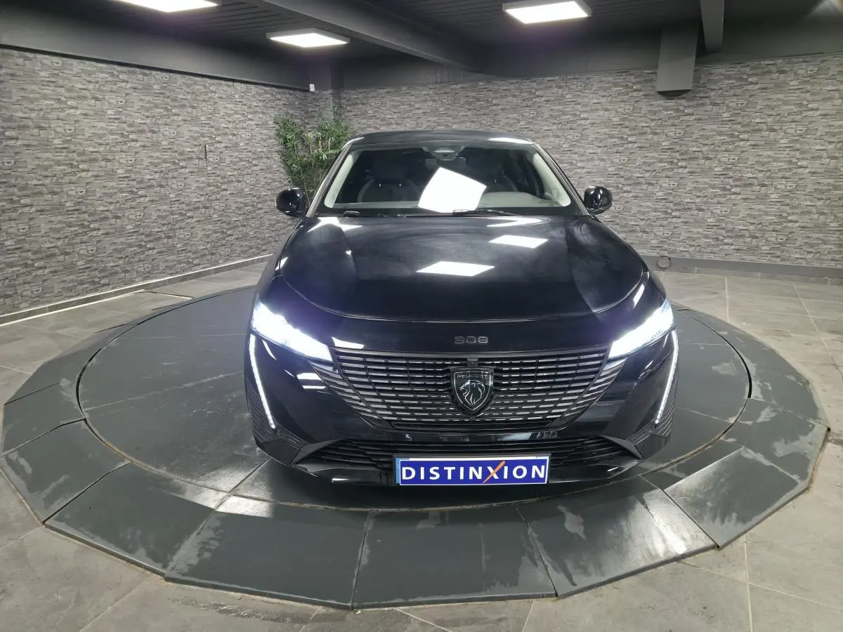 Peugeot 308 SW noire vue de face en intérieur, avec calandre noire et feux LED allumés.