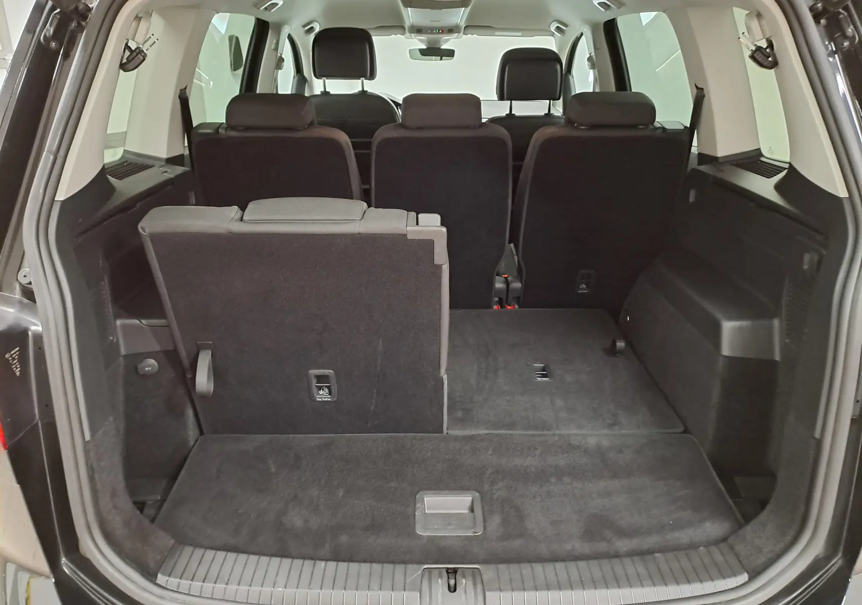 Vue arrière du coffre ouvert du Volkswagen Touran noir intense nacré, montrant les sièges arrière partiellement rabattus.