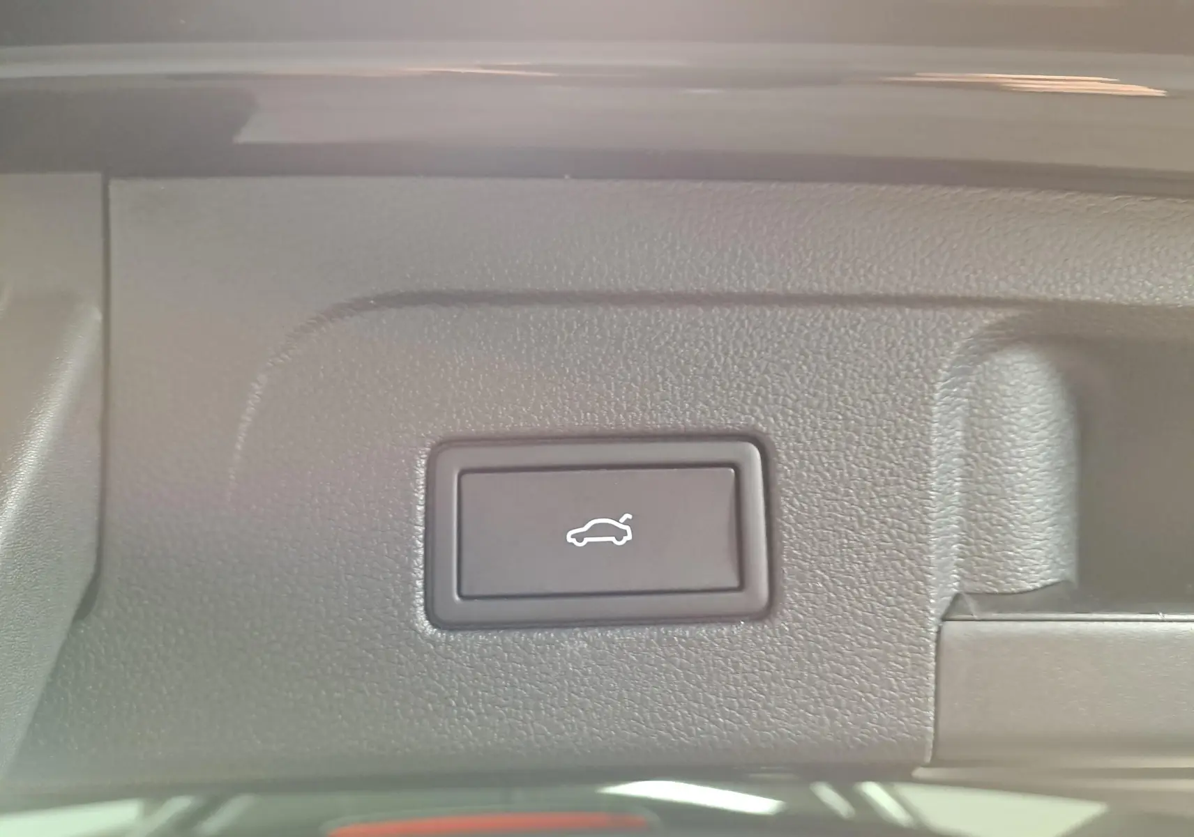 Bouton d'ouverture électrique du coffre sur la partie intérieure du hayon d'un Volkswagen Touran noir intense nacré.