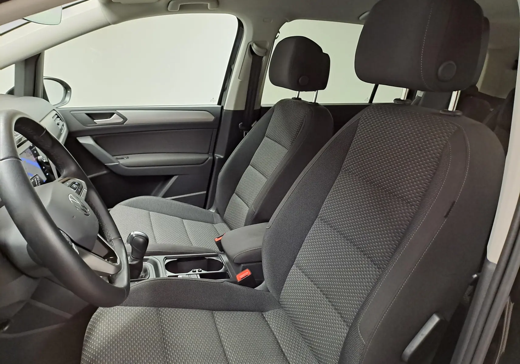 Vue intérieure côté conducteur du Volkswagen Touran 2025, sièges tissu gris et tableau de bord moderne.