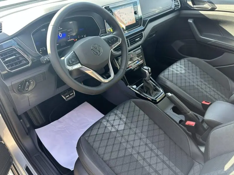 Vue intérieure côté conducteur du Volkswagen T-Cross 2025, avec volant multifonction, écran tactile et sièges tissu à motif géométrique.