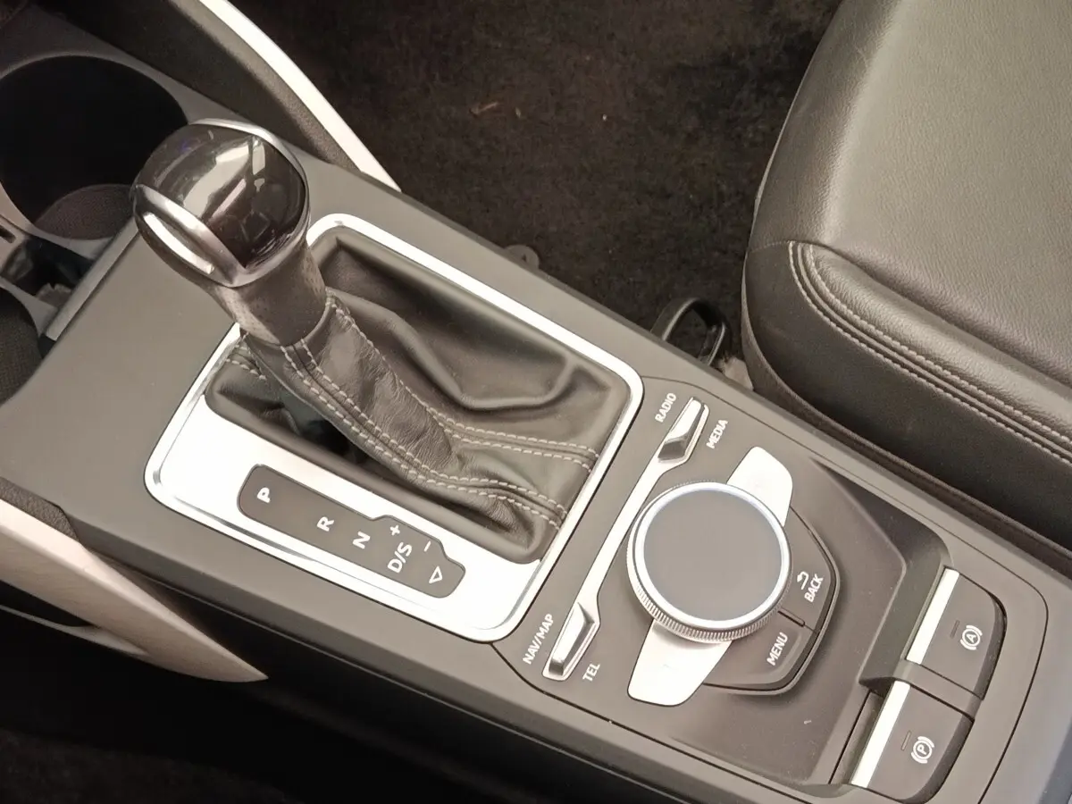 Gros plan sur la console centrale de l’Audi Q2 noire, avec levier de vitesse automatique et molette de commande multimédia.