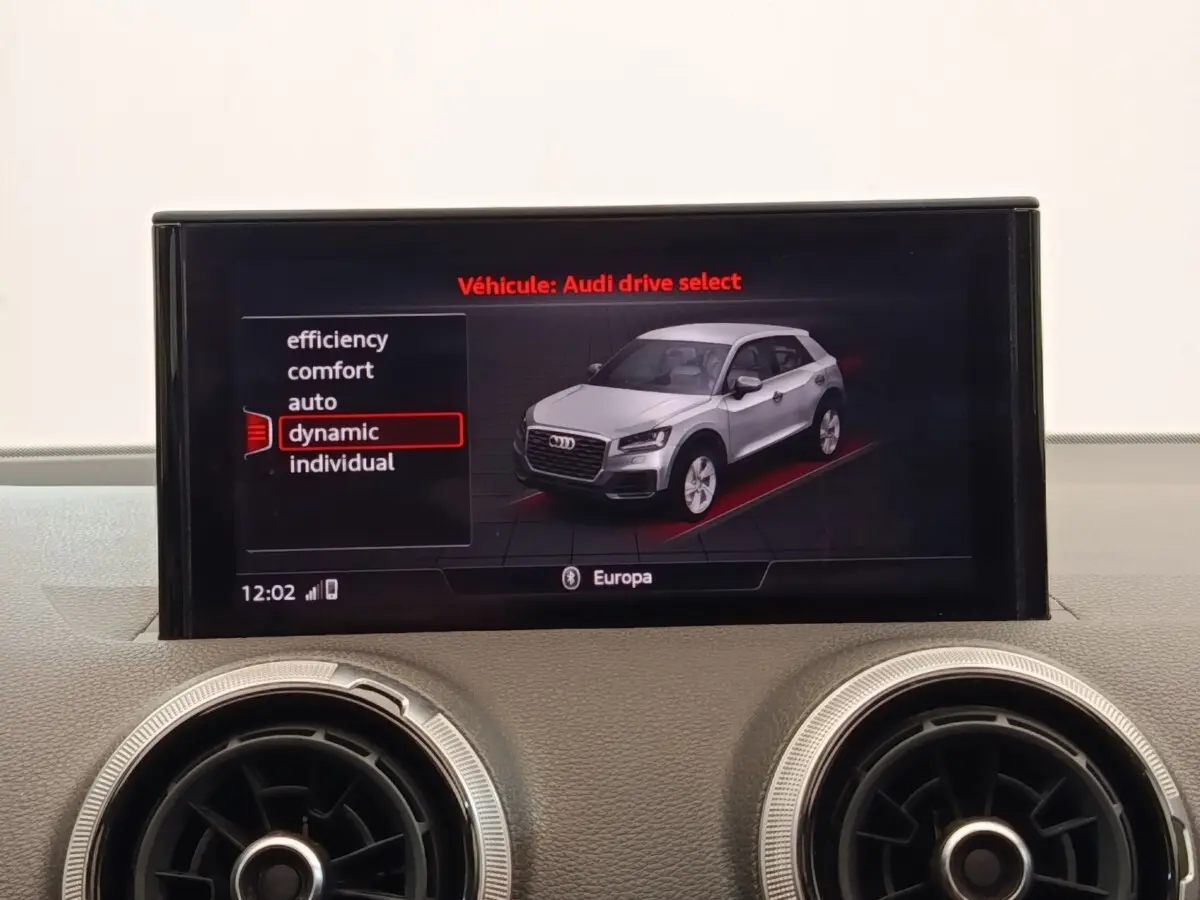 Écran central affichant le mode Audi drive select avec un SUV Q2 gris en vue 3/4 avant, entouré de commandes d’aération rondes.