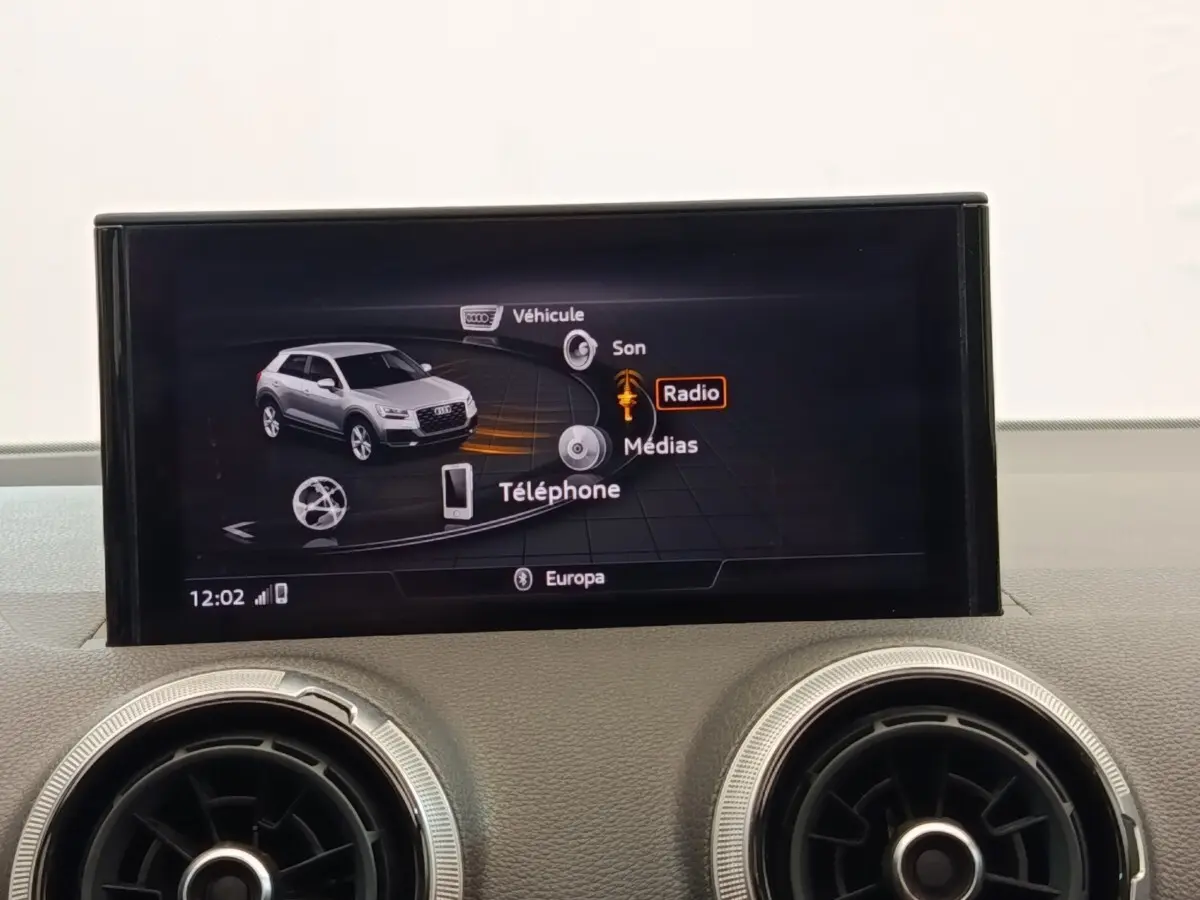 Écran tactile central affichant le menu multimédia d’un Audi Q2 noir, avec deux aérateurs ronds en dessous.