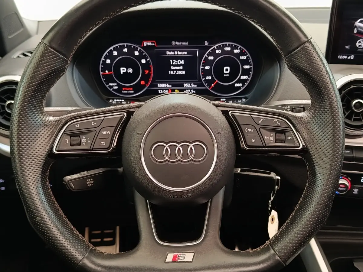 Vue rapprochée du volant cuir perforé Audi Q2 S Line 2021 avec tableau de bord numérique et commandes multifonctions.