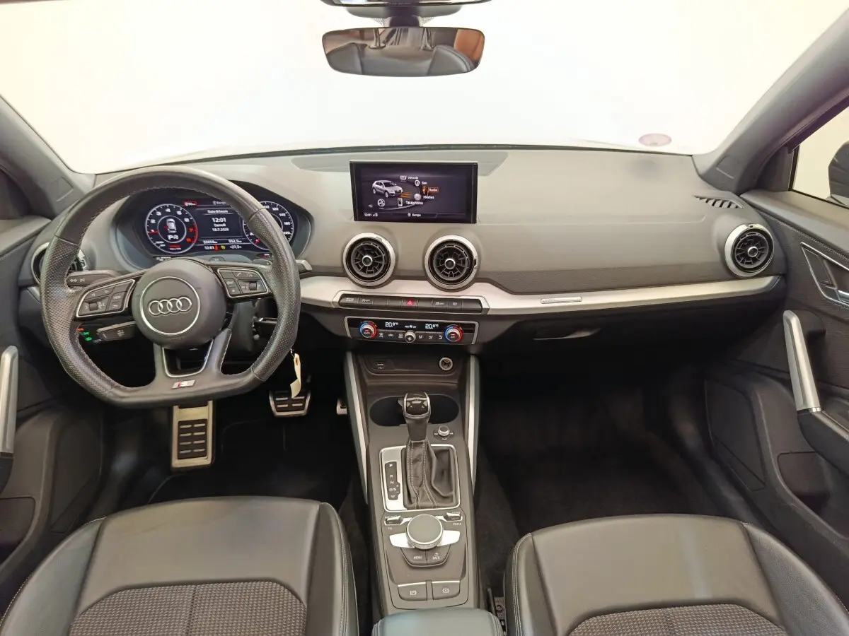 Vue intérieure avant de l'Audi Q2 noir 35 TFSI 150 S Tronic S Line, avec volant cuir multifonctions et écran central tactile.