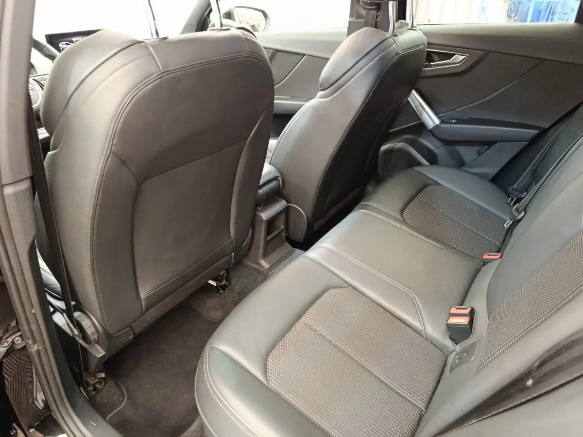 Vue intérieure arrière côté gauche de l’Audi Q2 noir, mettant en valeur la banquette 3 places en cuir et les sièges avant.