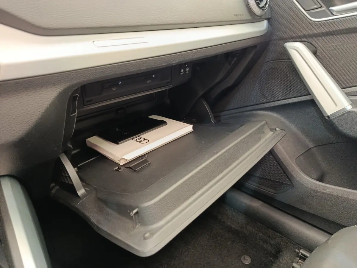 Gant de boîte à gants ouvert côté passager dans l'Audi Q2 noir, avec manuel et porte-CD visibles.