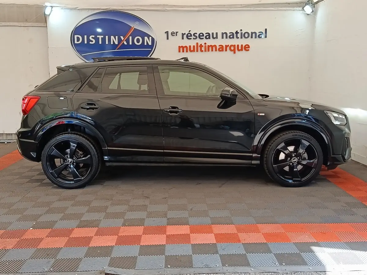 Profil côté gauche d'un Audi Q2 noir 35 TFSI S Line 2021 avec jantes noires dans un showroom multimarque.