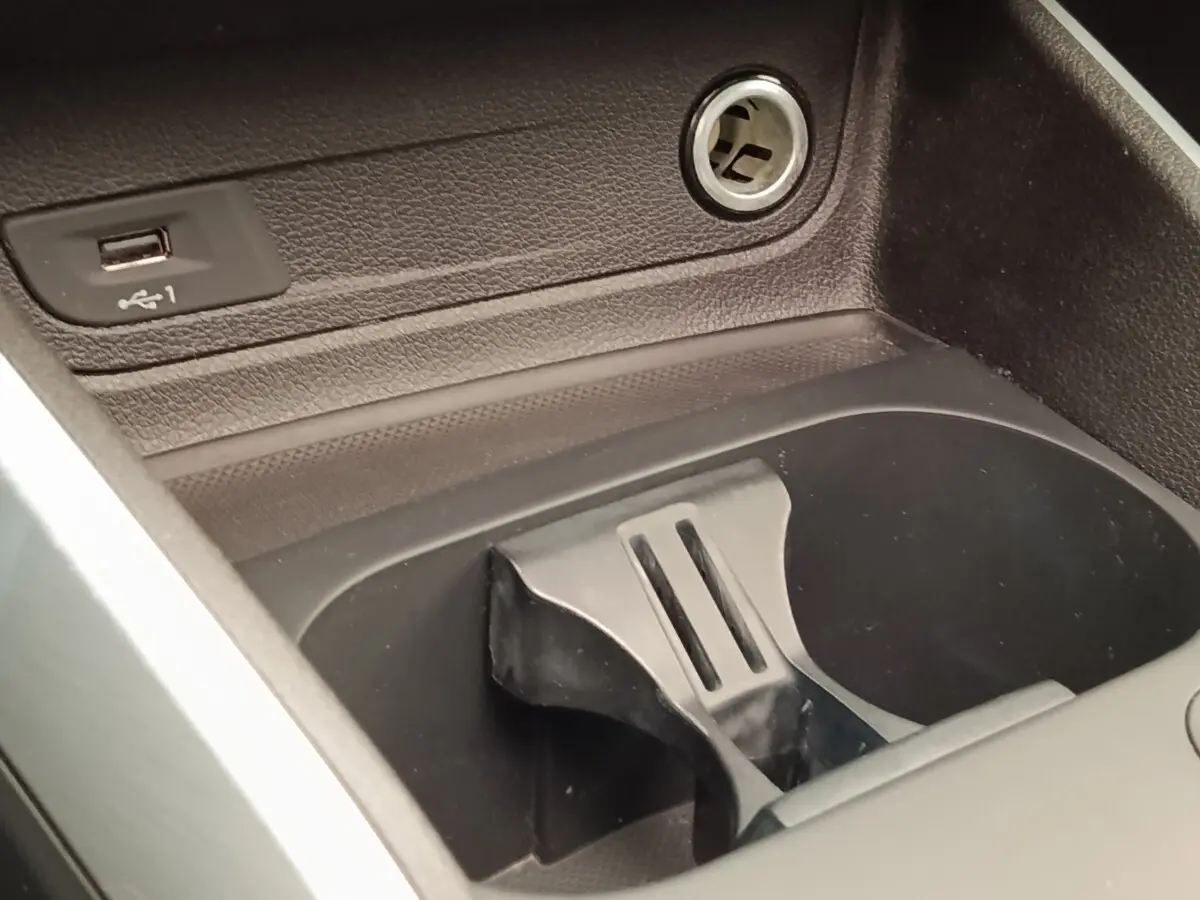 Gros plan sur la console centrale noire de l’Audi Q2, montrant un port USB et un porte-gobelets intégré.