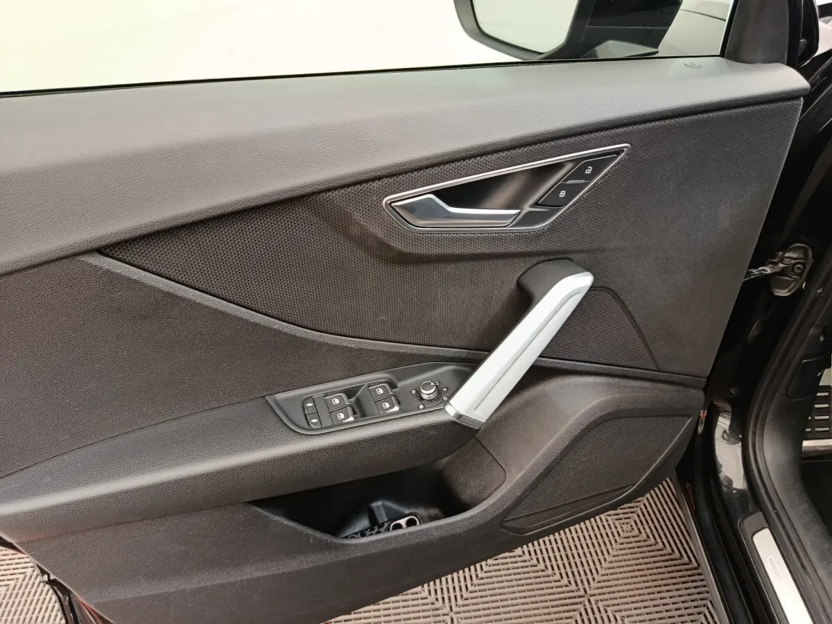 Vue rapprochée de la porte avant gauche noire d'un Audi Q2 35 TFSI S Line, avec commandes de vitres et poignée argentée.