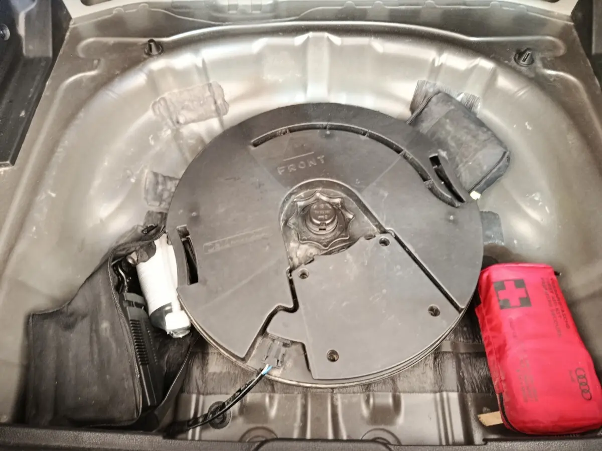Vue plongeante sur le coffre d’un Audi Q2 noir 2021, montrant la roue de secours et une trousse de secours rouge.
