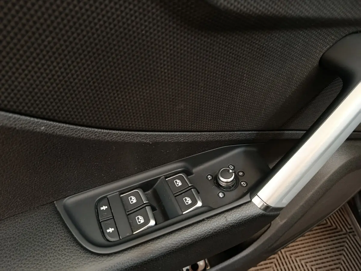 Gros plan sur les commandes des vitres et rétroviseurs côté conducteur de l'Audi Q2 noir, intérieur porte avant.