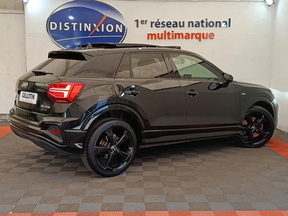 Audi Q2 35 TFSI S Line noir en vue profil côté droit, avec jantes noires et vitres teintées, en intérieur showroom.