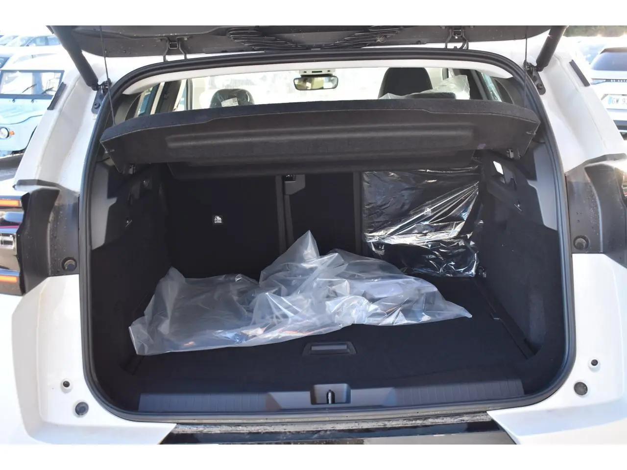 Coffre ouvert d'un Citroën C5 Aircross blanc, vue arrière, montrant l'espace de chargement avec couverture de protection noire.