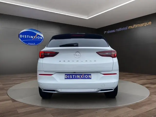 Vue arrière d'un Opel Grandland blanc Arktis avec toit noir, feux LED et logo distinctif sur fond showroom.
