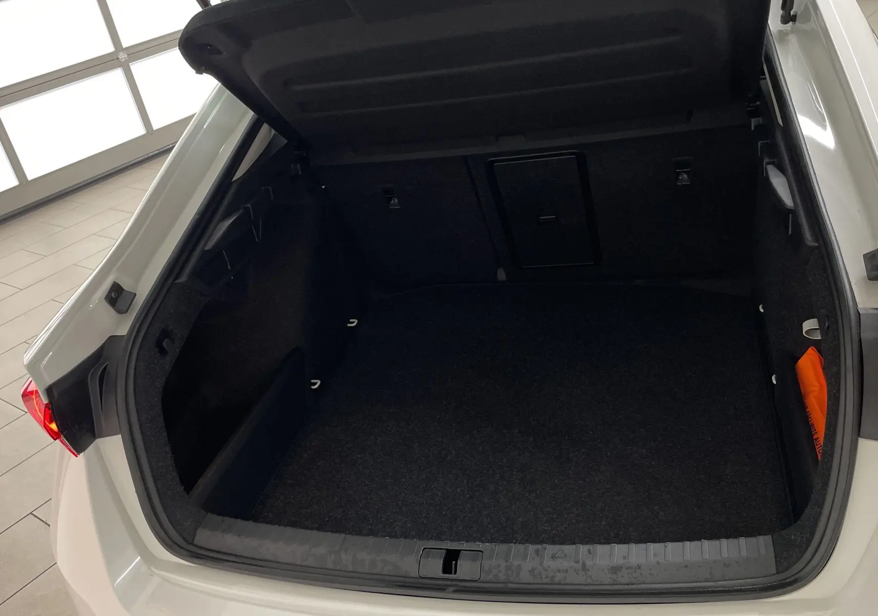 Coffre ouvert vu de l'arrière d'une Skoda Octavia blanc candy 2024 avec roue de secours galette visible sous la moquette.