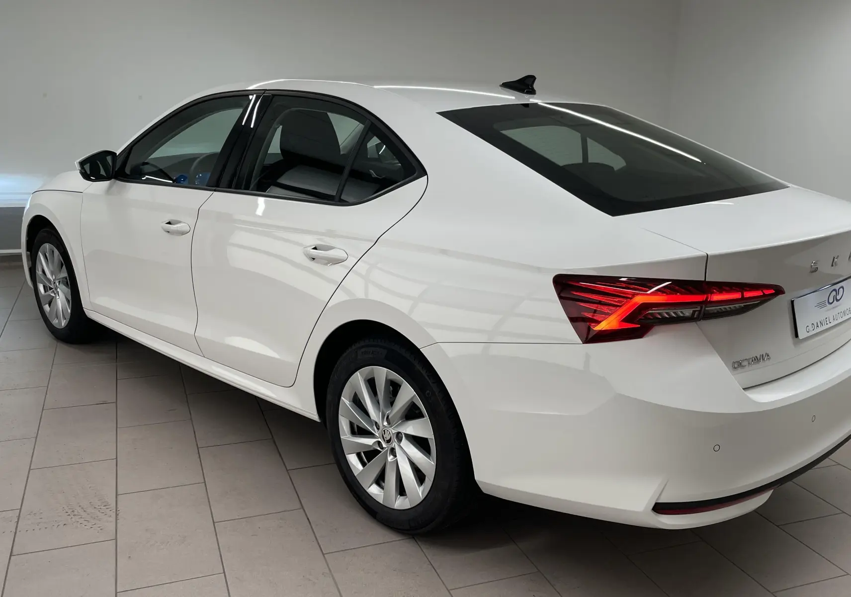 Vue 3/4 arrière droite d'une Skoda Octavia 2024 blanche Candy avec feux arrière allumés et jantes alliage.