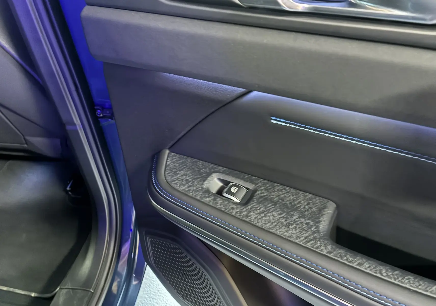 Vue rapprochée de la porte arrière gauche bleu du Lynk & Co 01 2023 avec couture bleue et bouton de lève-vitre.