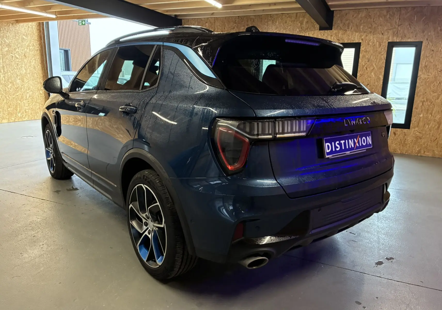 Vue 3/4 arrière droite d'un SUV Lynk & Co 01 bleu avec feux arrière LED et jantes alliage bicolores.