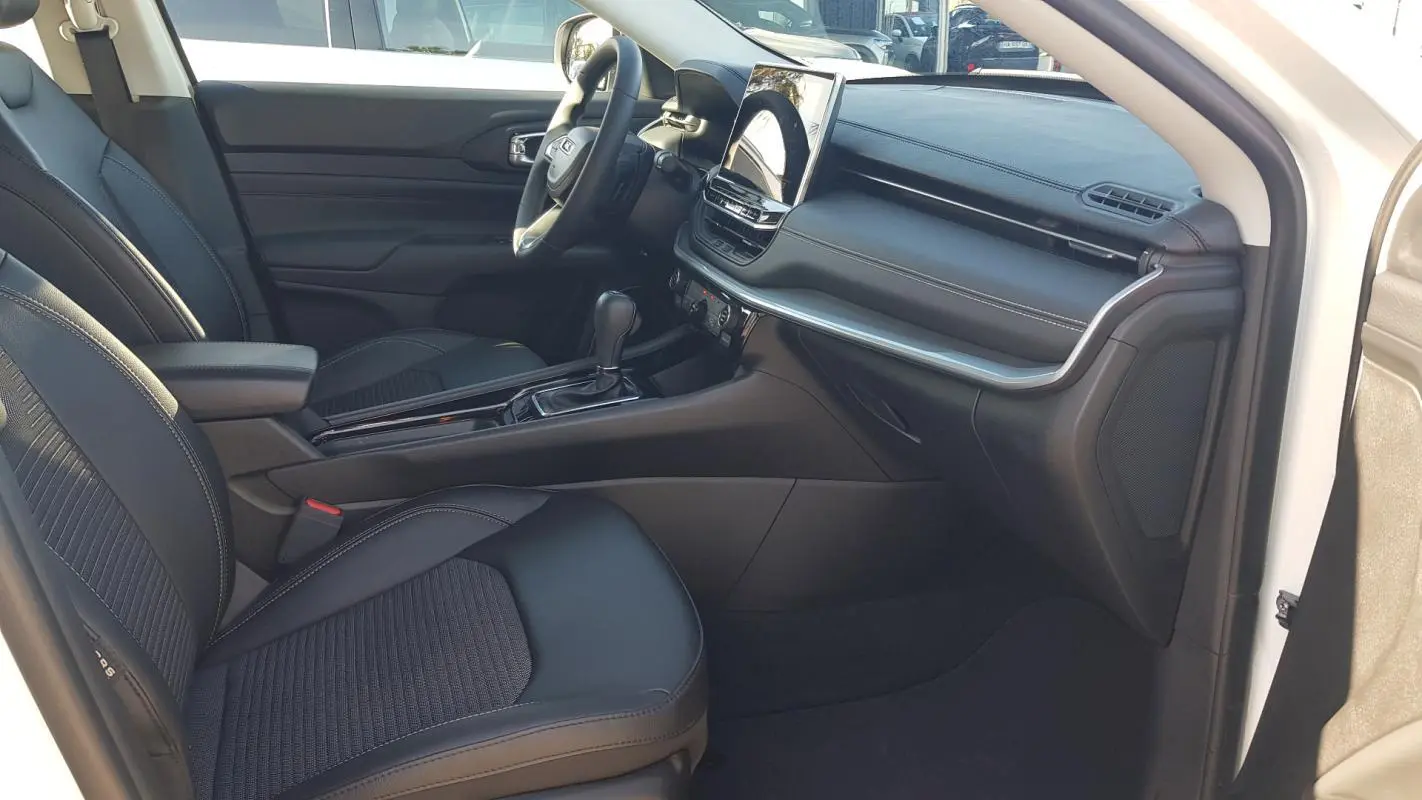 Vue intérieure côté conducteur du Jeep Compass blanc 2024, montrant siège noir, tableau de bord et écran tactile central.