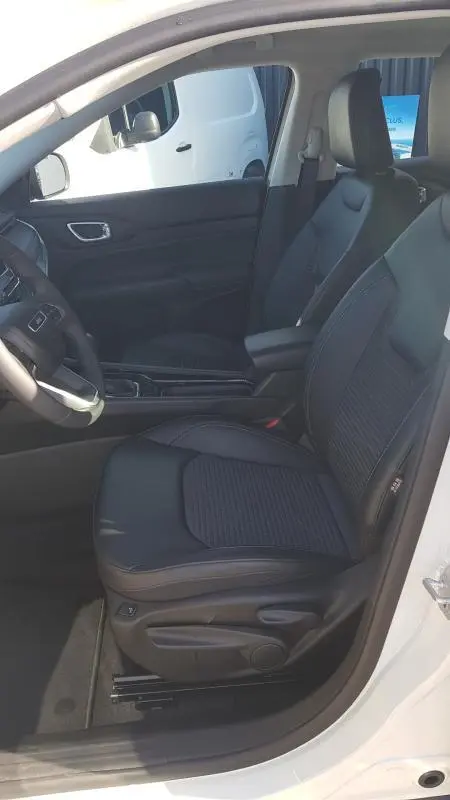 Vue intérieure côté conducteur du Jeep Compass blanc 2024, mettant en valeur les sièges noirs et l'accoudoir central.