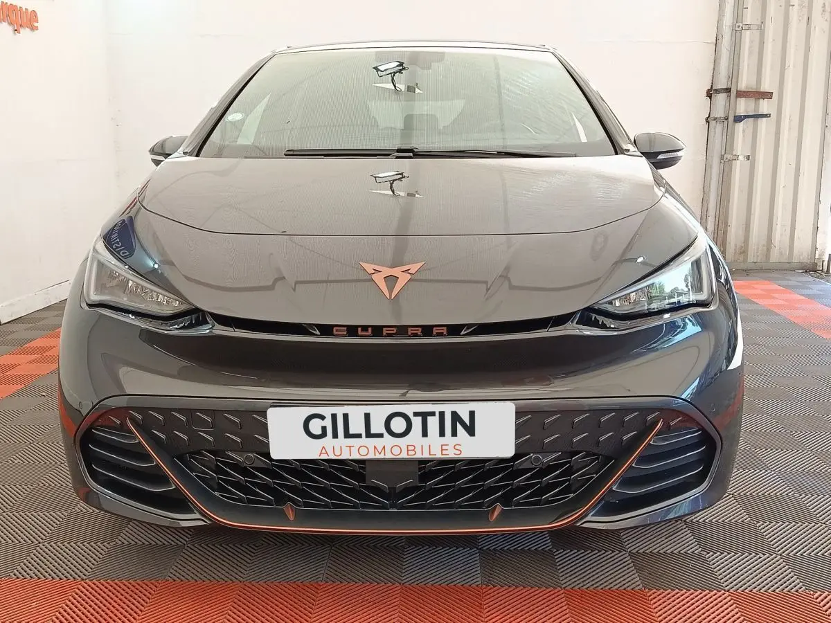 Vue avant d'une CUPRA Born gris foncé avec logo cuivre et calandre noire soulignée d'orange dans un showroom.