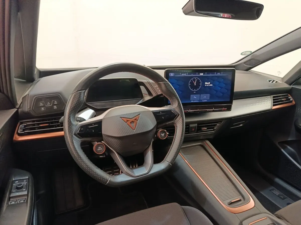 Vue intérieure avant du CUPRA BORN gris foncé, volant cuir avec logo, grand écran tactile central et détails cuivrés sur la planche de bord.