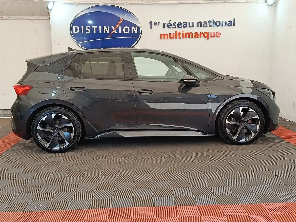 Profil droit de la CUPRA BORN 230ch gris foncé électrique 2023 avec jantes noires et logo distinctif sur roue.