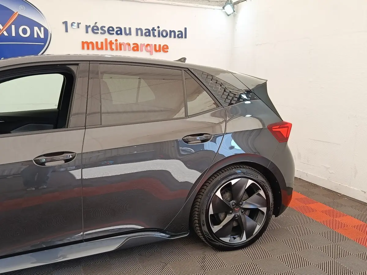 Vue latérale droite du CUPRA Born gris foncé, mettant en valeur la roue arrière et les lignes dynamiques du véhicule.