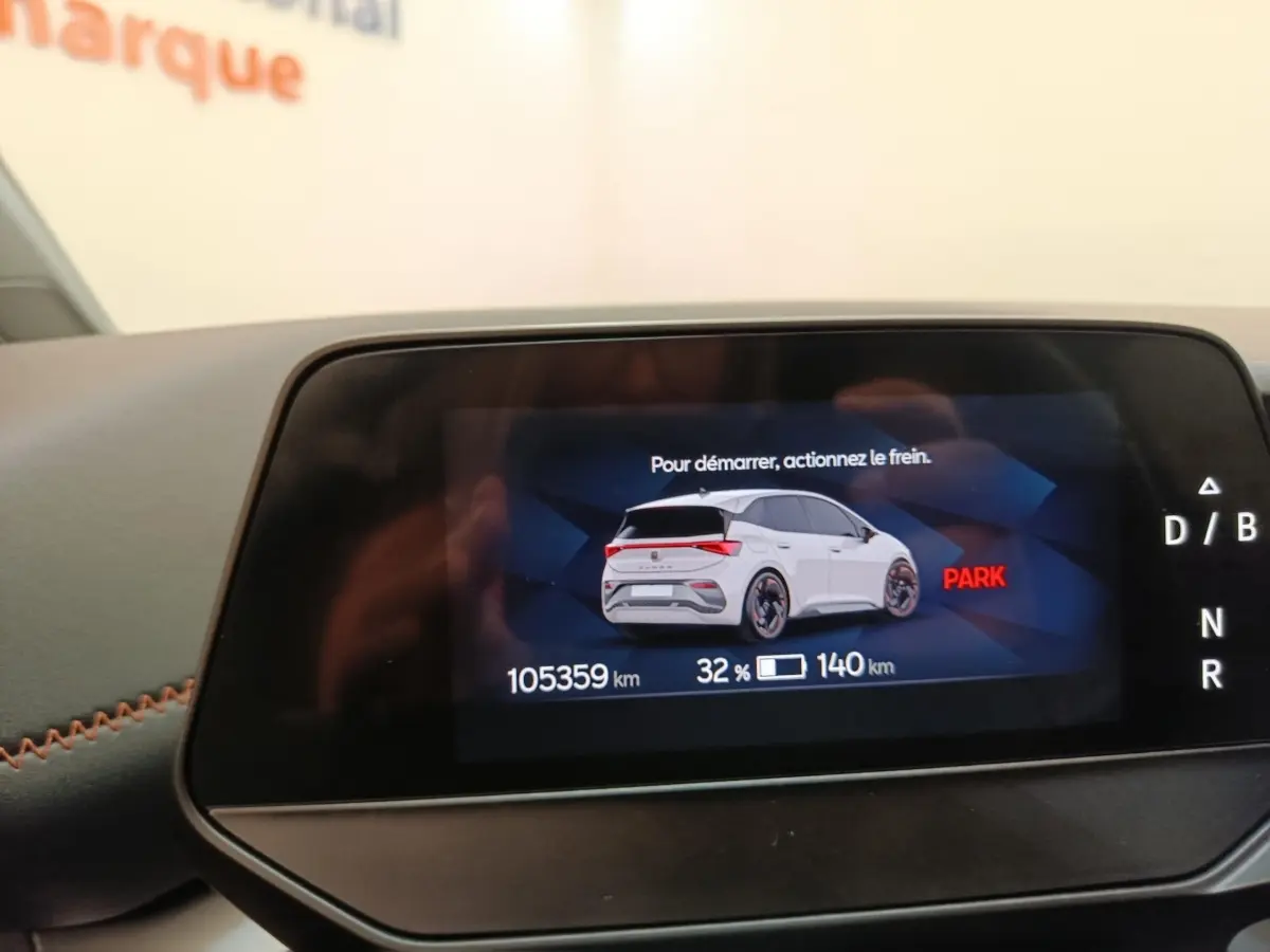 Écran numérique montrant une CUPRA Born blanche en vue arrière 3/4 avec indicateur de charge et kilométrage.