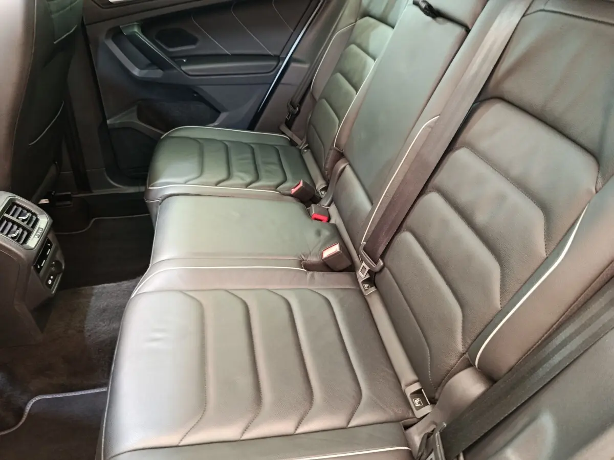Vue latérale intérieure des sièges arrière en cuir noir du Volkswagen Tiguan 1.4 eHybrid 2023, avec ceintures et aérateurs.