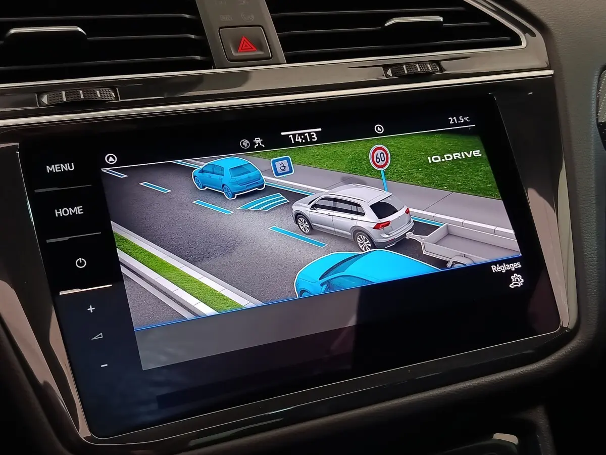 Écran tactile central montrant l'aide à la conduite avec représentation graphique d'un Volkswagen Tiguan blanc en circulation.