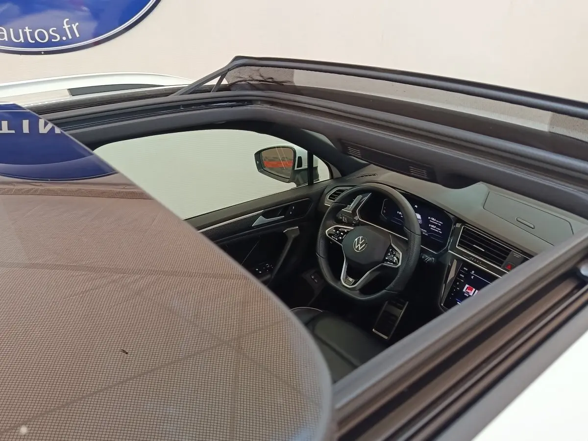 Vue intérieure par le toit ouvrant du Volkswagen Tiguan blanc 2023, montrant le volant multifonctions et le tableau de bord digital.