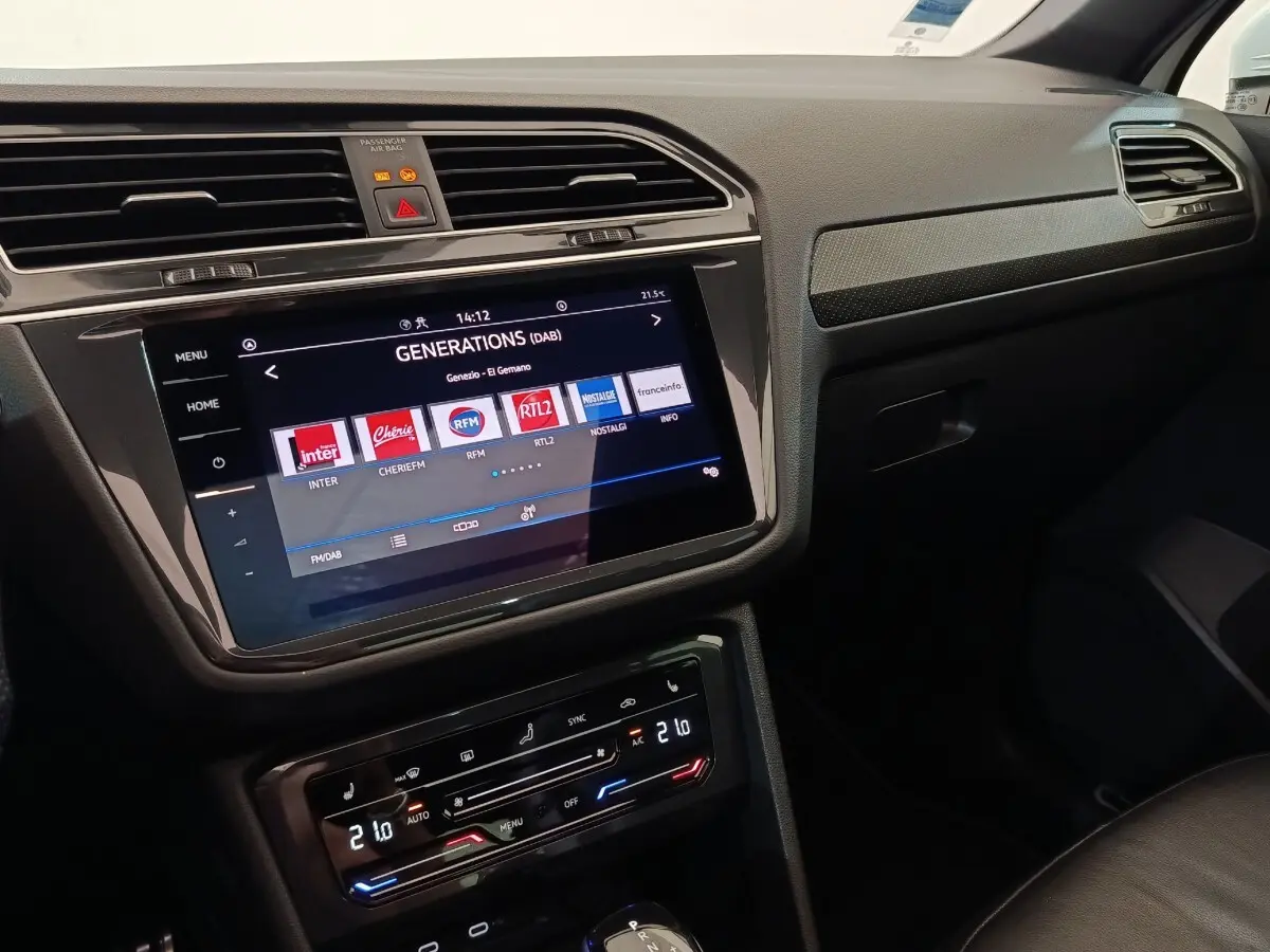 Vue intérieure du tableau de bord du Volkswagen Tiguan blanc 2023, écran tactile central et commandes climatisation visibles.