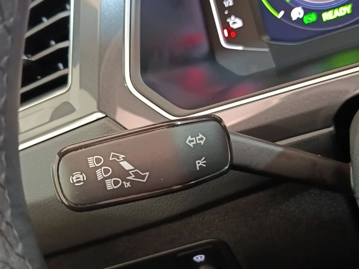 Gros plan sur la manette de clignotant et feux du Volkswagen Tiguan hybride, tableau de bord numérique en arrière-plan.