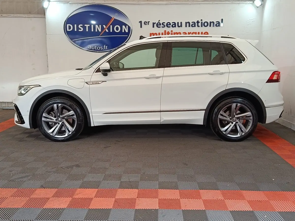 Profil droit d'un Volkswagen Tiguan blanc 2023 hybride rechargeable finition R-Line Exclusive avec jantes alliage et toit ouvrant.